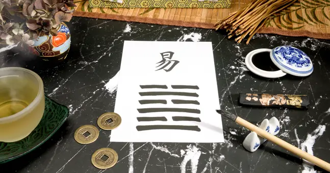 Close-up of an I Ching setup featuring the 63rd hexagram, After Completion (Chi Chi), written with a Chinese ink brush on rice paper. Yarrow stalks and a traditional Chinese ink tank highlight the process of interpreting changing lines in a step-by-step I Ching guide.